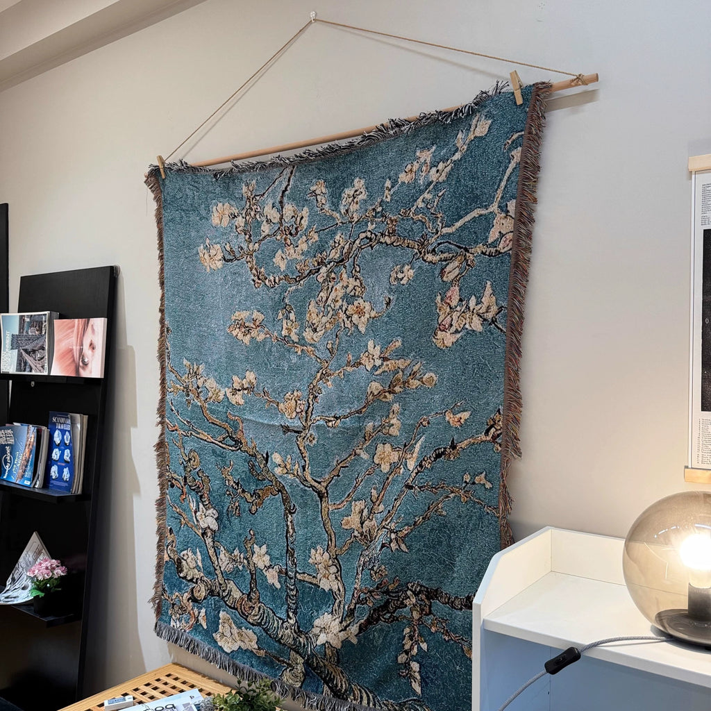 Wall tapestry with floral design hanging on a wall next to a shelf and lamp.